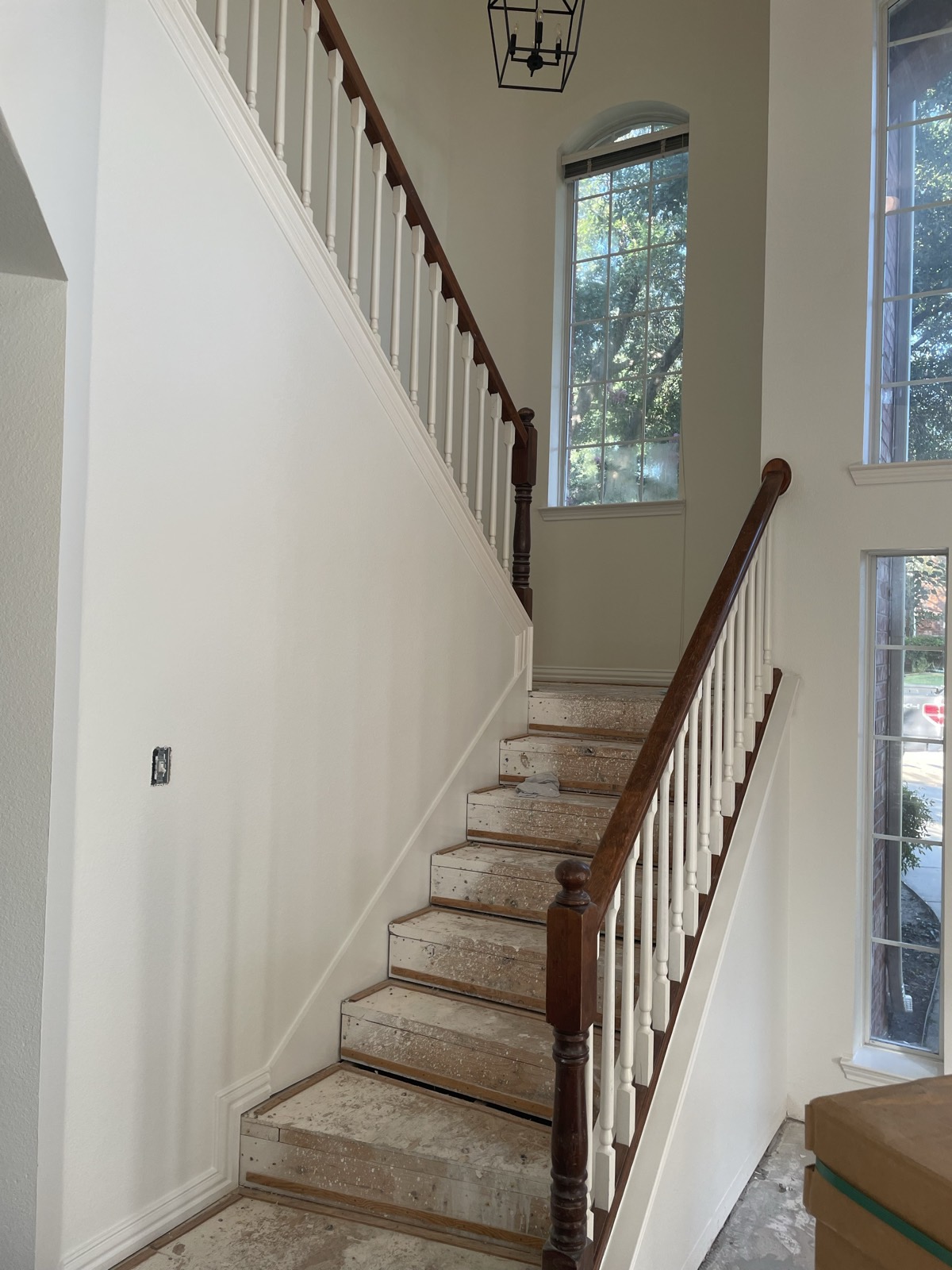 Refinished staircase with stained handrail, white balusters, and arched window
